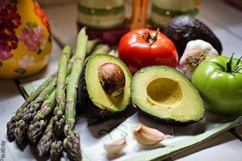 Gesunder Gem&uuml;seteller bestehend aus einer aufgeschnittenen Avocado, zwei ganze Tomaten in rot und gr&uuml;n, gr&uuml;nem Spargel und zwei Knoblauchzehen