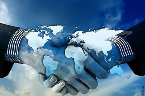 Zwei Personen, die sich die H&auml;nde sch&uuml;tteln. Der Bildausschnitt zeigt nur die H&auml;nde, die durch eine blau-wei&szlig;e Weltkarte angeleuchtet werden.