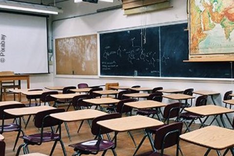 Ein leerer Seminarraum mit einer beschrifteten Tafel, einer ausgefahrenen Leinwand und einer ausgeklappten Weltkarte