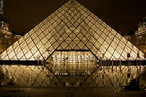 Frontalansicht des Kunstmuseums Louvre im - Dunkeln hell erleuchtet.