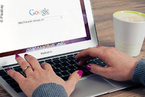 Internet - Google Frauenhände tippen auf einem Laptop. Auf dem Bildschirm ist die Startseite von Google zu sehen.